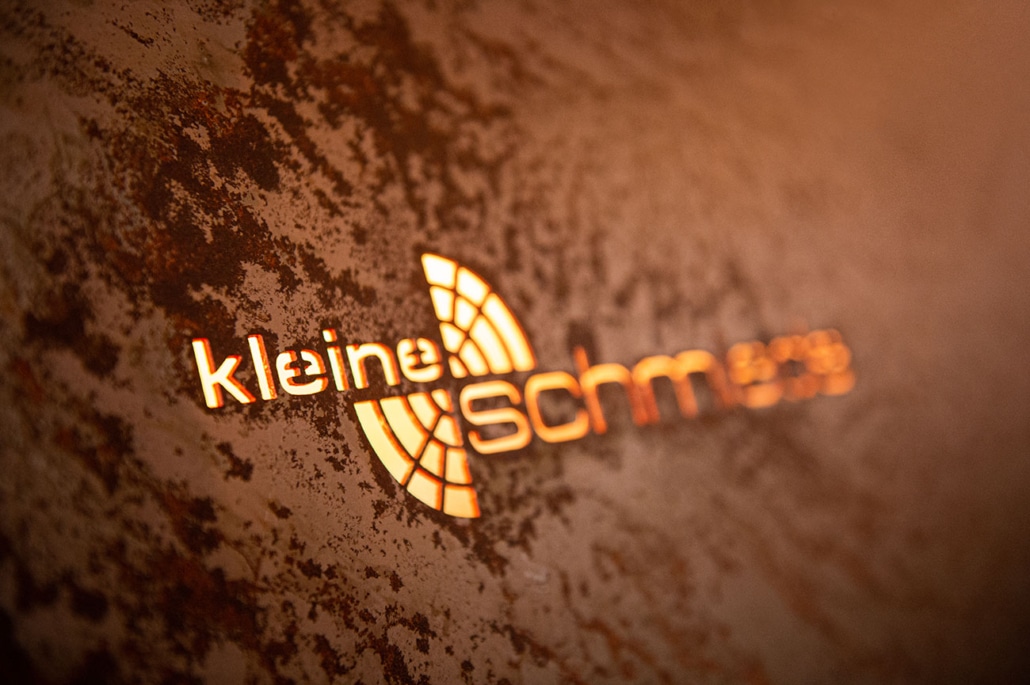 Beleuchtetes Logo der Kleinen Schmiede auf einer rustikalen Metallwand in der Eventlocation in Unna.