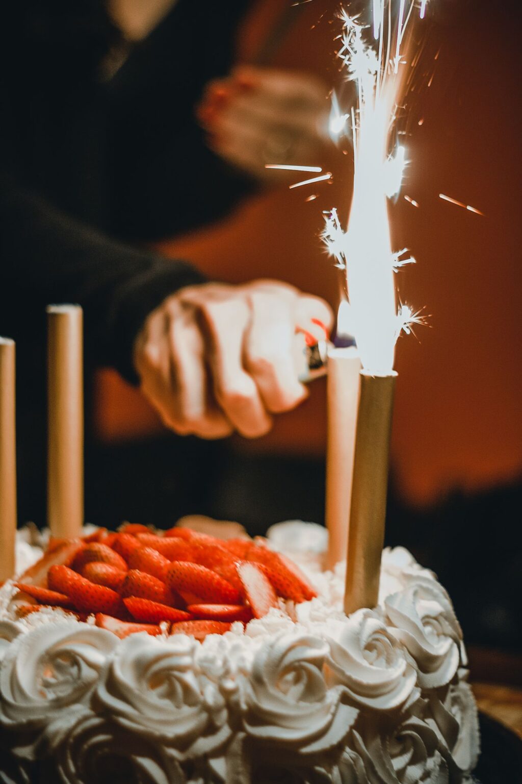 Festliche Geburtstagstorte mit Erdbeeren und brennender Funkenkerze bei einer Feier.