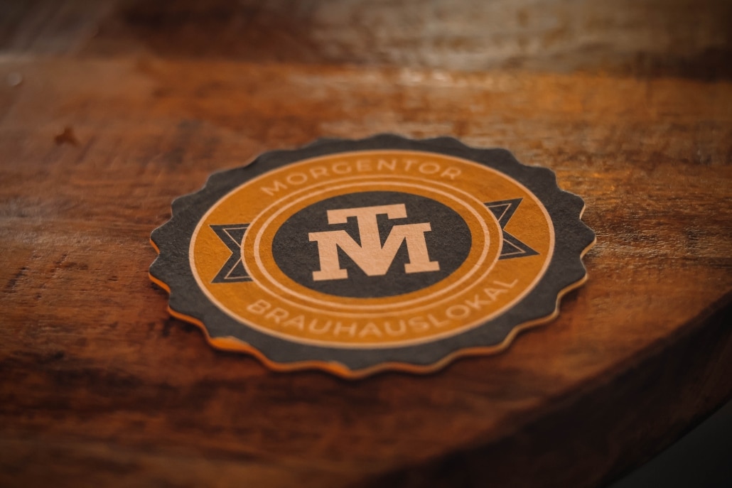 Bierdeckel mit dem Logo des Morgentors auf einem rustikalen Holztisch.
