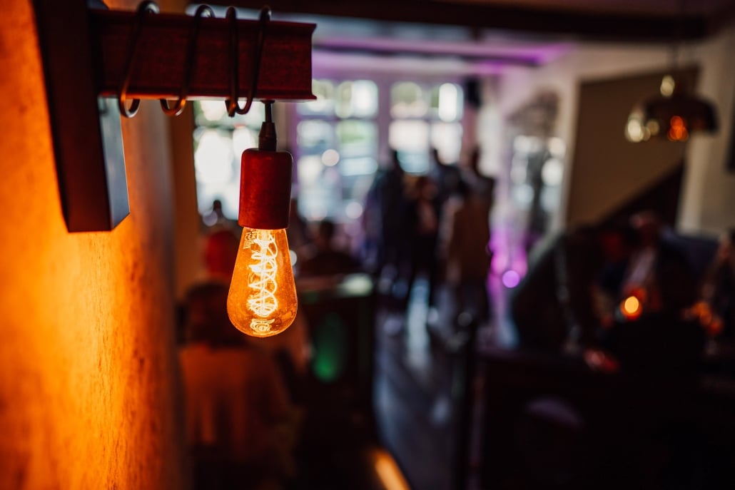 Leuchtende Edison-Lampe im Morgentor in Unna mit stimmungsvoll beleuchtetem Gastraum im Hintergrund.
