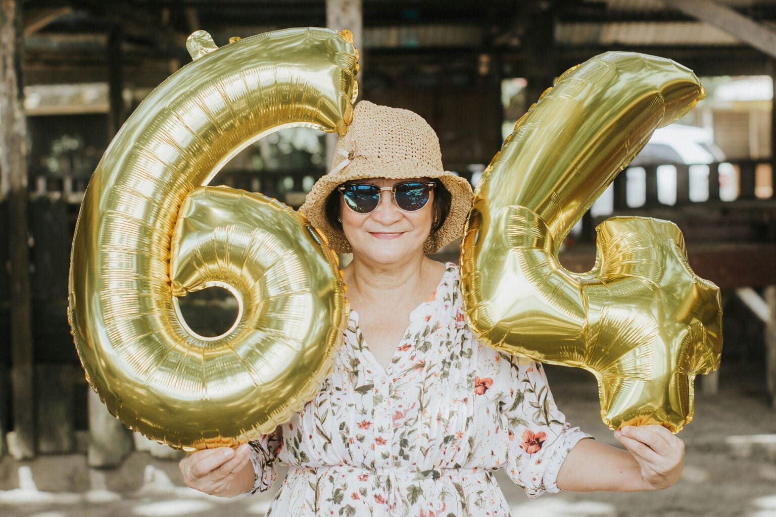 Person hält goldene Luftballons mit der Zahl 64 für eine Geburtstagsfeier in einer Eventlocation.