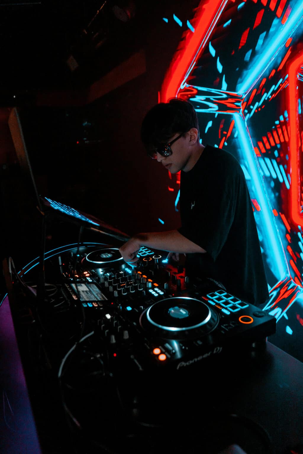 DJ legt an einem professionellen Mischpult in einer modernen Eventlocation mit Neonbeleuchtung auf.
