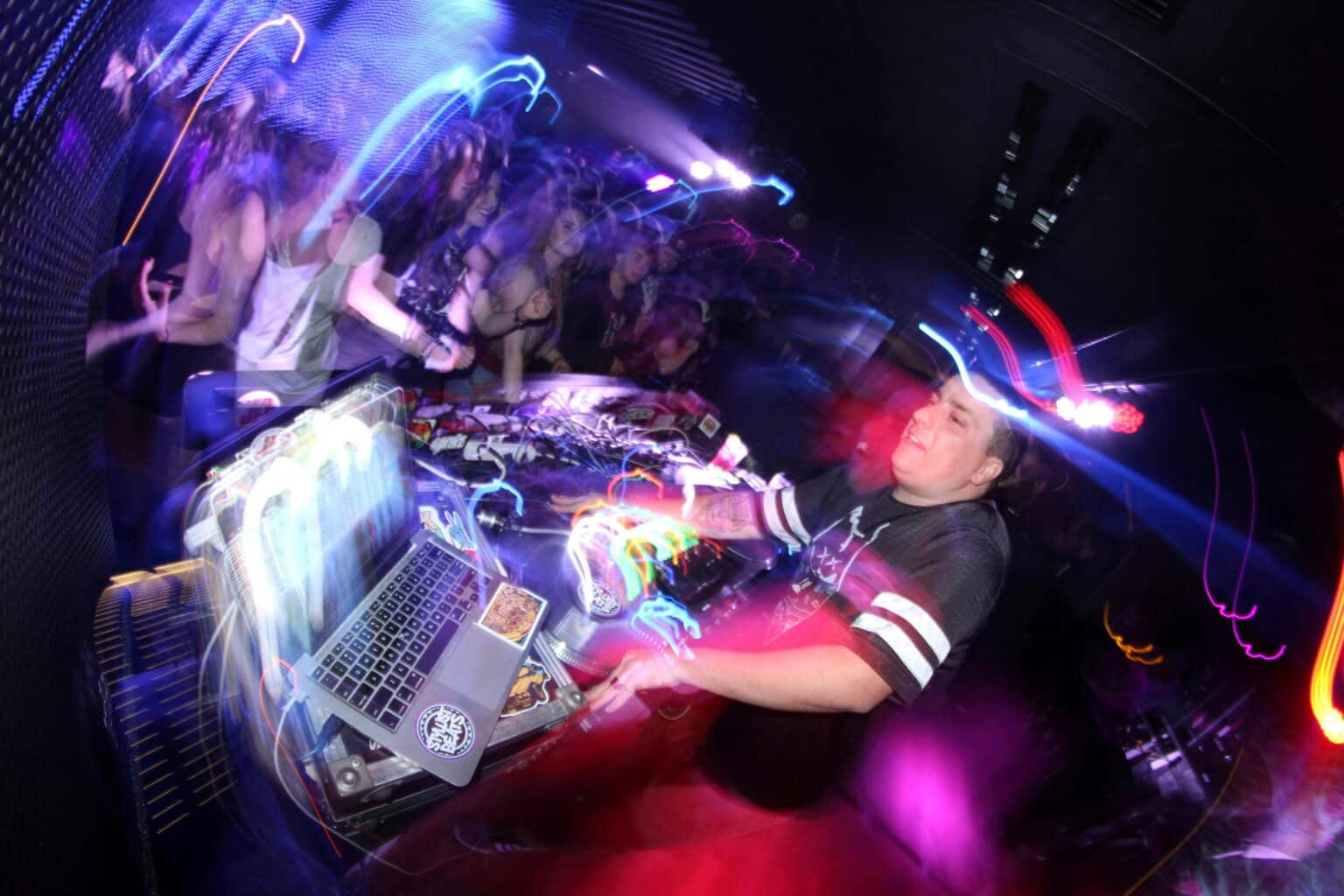 DJ legt bei einer Party auf, während Gäste vor der Bühne tanzen.