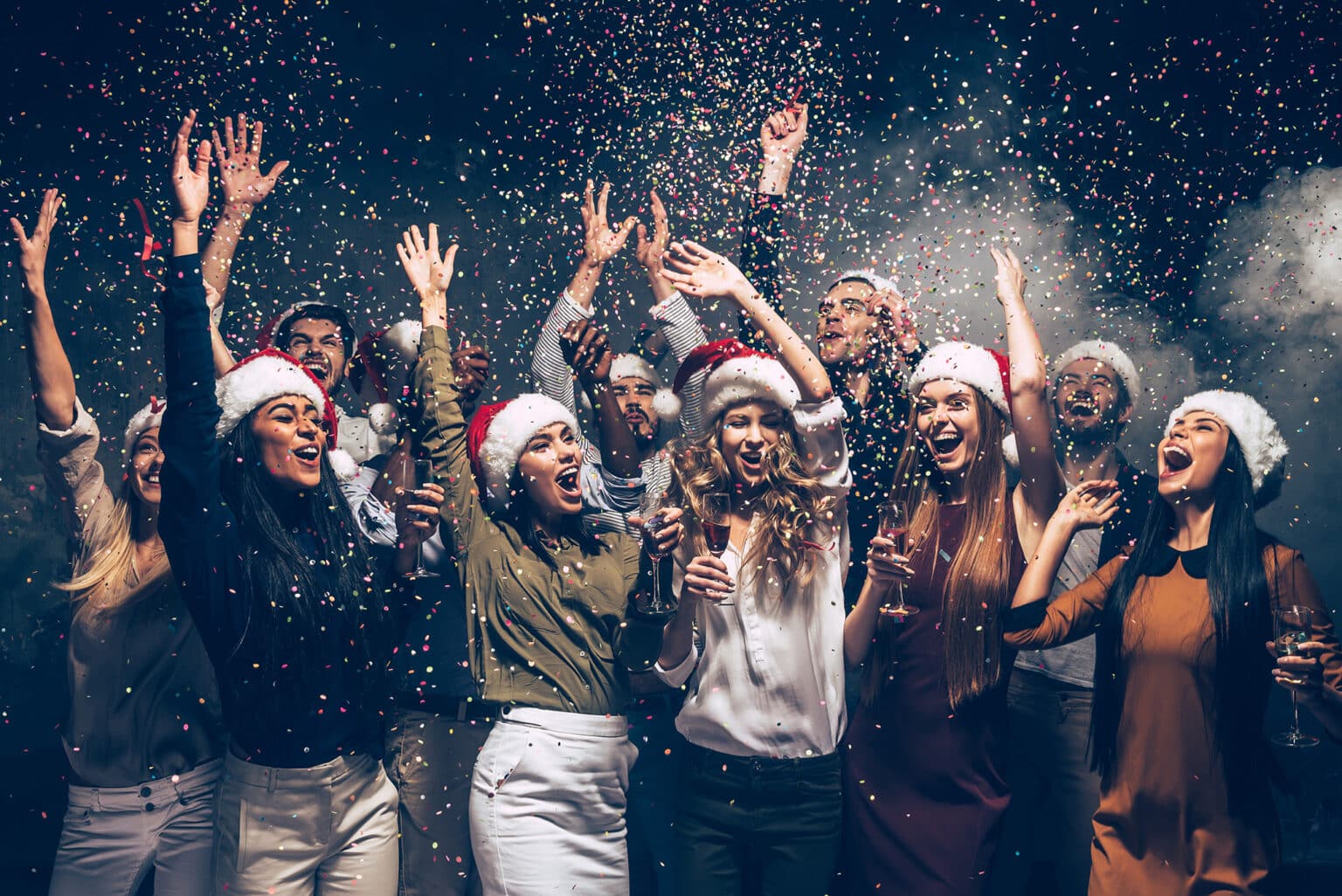 Gruppe feiert ausgelassen auf einer Weihnachtsfeier mit Konfetti und Weihnachtsmützen.
