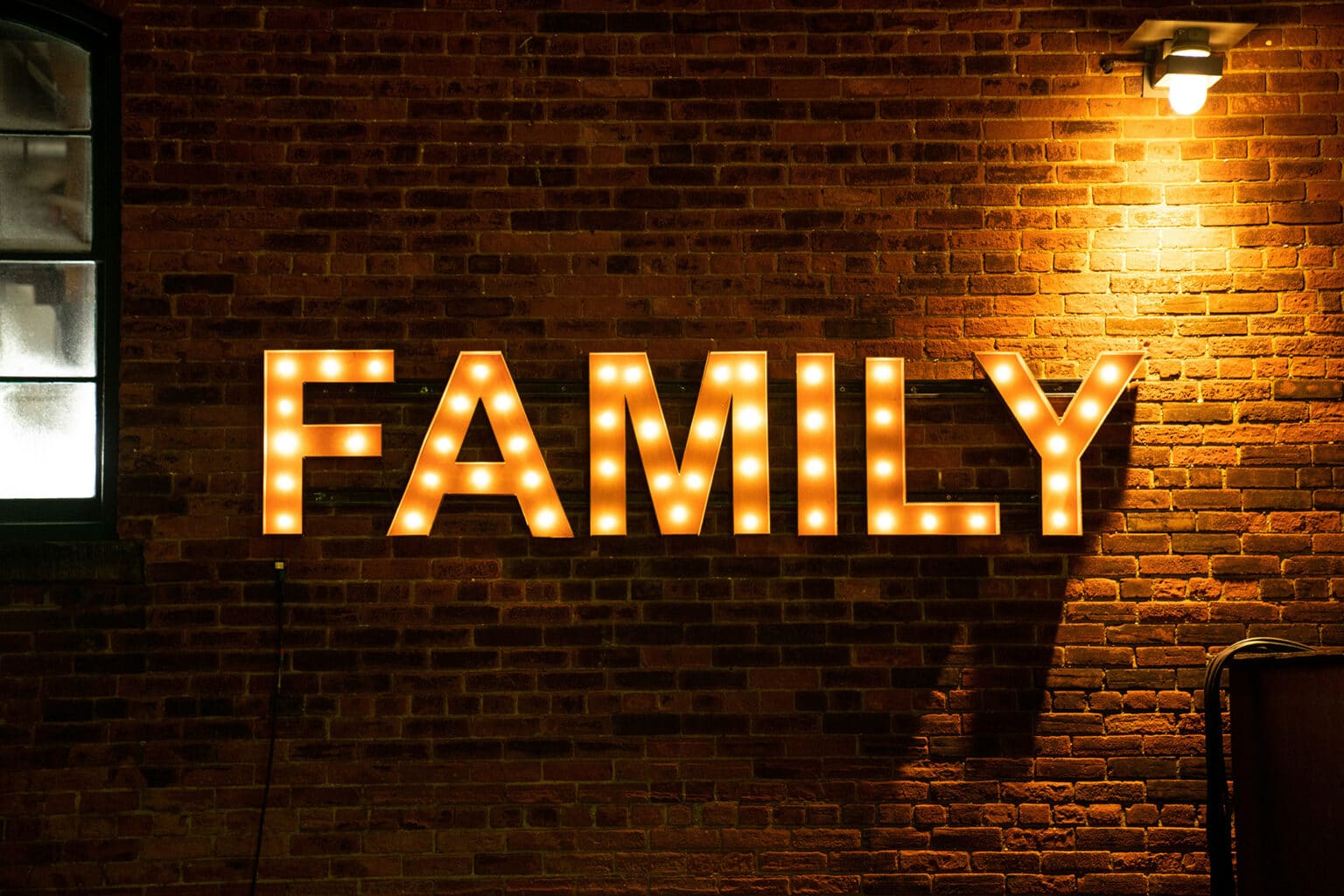 Leuchtender Schriftzug „Family“ an einer Backsteinwand als Dekoration für eine Familienfeier in einer Eventlocation.
