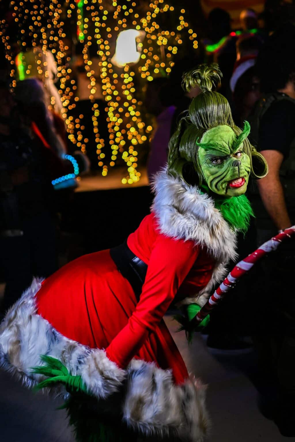 Person im Grinch-Kostüm auf einer weihnachtlichen Party mit Lichterketten und festlicher Atmosphäre.